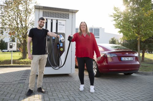 Alexander Sohl und Ines Adler vom Unternehmen ME Energy halten Ladekabel für Elektro-Fahrzeuge in der Hand. Im Hintergrund ein Elektro-Auto neben einer Elektro-Ladesäule.