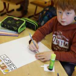 Ein Junge im Grundschulalter sitzt an einem Schultisch mit Arbeitsmaterialien.