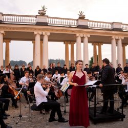 Schloss Rheinsberg. Eine Sängerin steht vor einem Orchester auf einer Open-Air-Bühne.