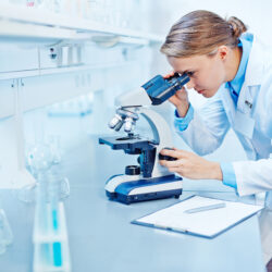 Ein Arbeitsplatz in einem Labor. Eine Mitarbeiterin schaut durch ein Mikroskop.