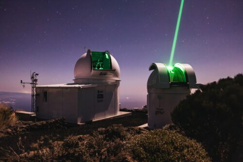 Eine astronomische Station auf einem Berg sendet einen grünen Laserstrahl in den Nachthimmel.