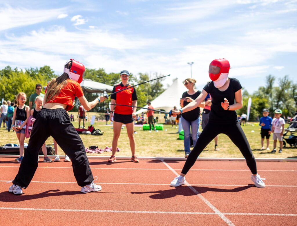Jugendliche auf dem Sportplatz beim Fechten.