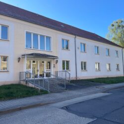 Außenansicht eines zweigeschossigen Funktionsgebäudes mit heller Fassade und einem behindertengerechten Eingang.